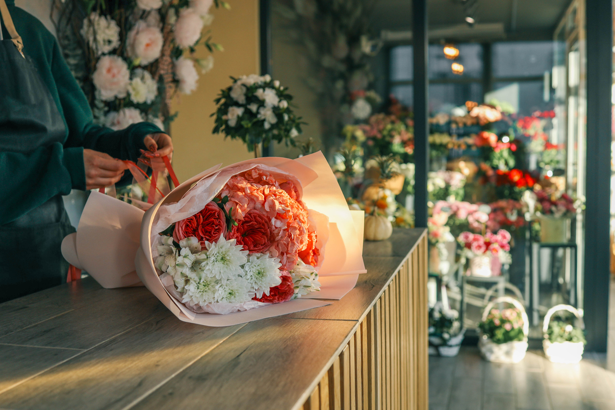 close-up-of-a-luxurious-bouquet-featuring-vibrant-red-roses-delicate-hydrangeas-and-white-alstroemerias-elegantly-arranged-and-wrapped-in-soft-pastel-paper-on-a-wooden-counter